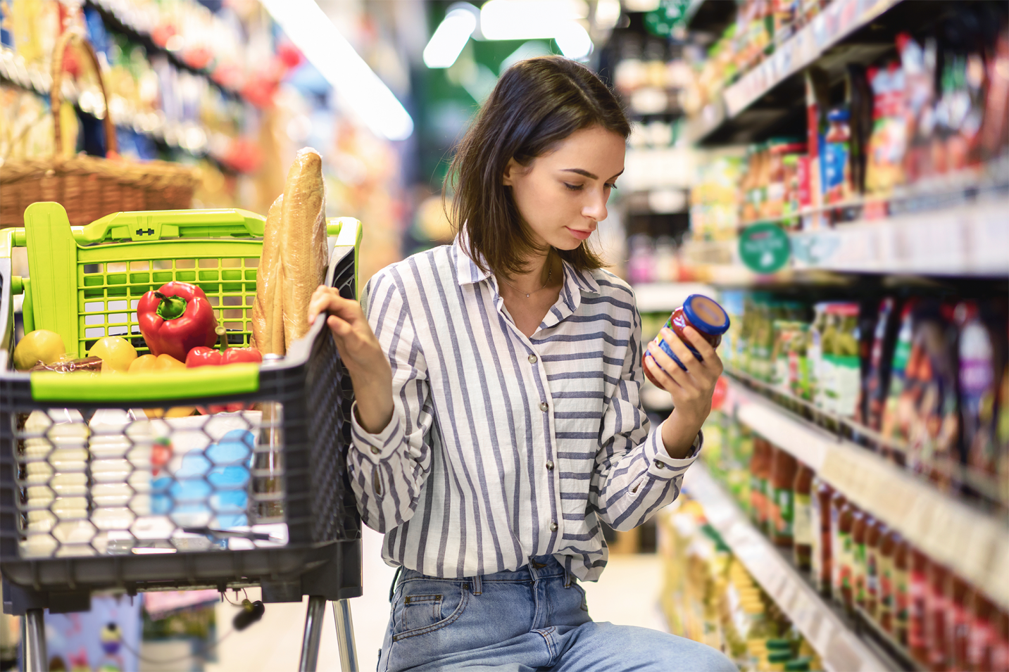 Mulher agachada lendo o rótulo nutricional de um produto em um supermercado.